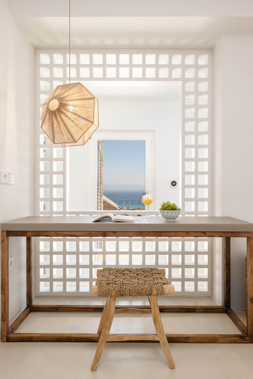 Minimalist white room with wooden desk and lattice window overlooking the sea.