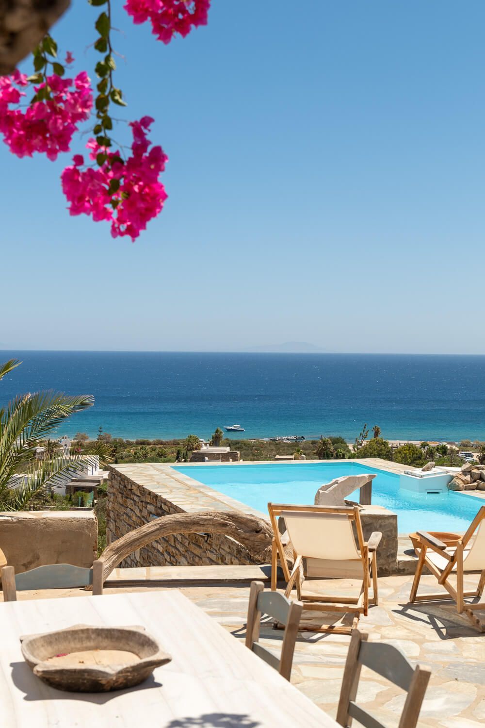 Infinity pool framed by vibrant bougainvillea at a picturesque Greek island property.