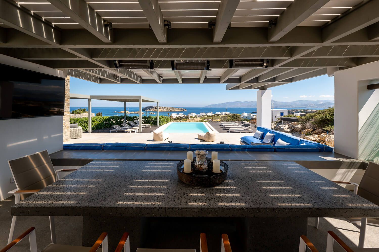 Luxurious covered patio with dining table overlooking infinity pool and turquoise ocean views in Mediterranean villa.