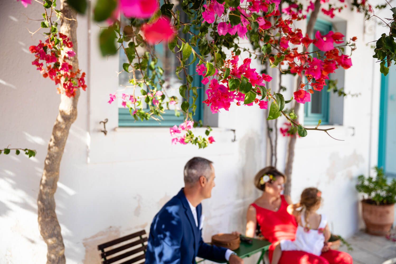 Couple with child seated under vibrant pink bougainvillea in Lefkes village.