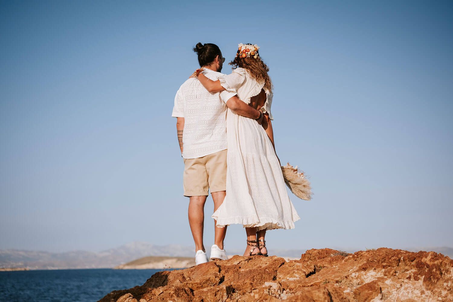 Wide shot of a boho couple standing on the hills of Pyrgaki before their wedding