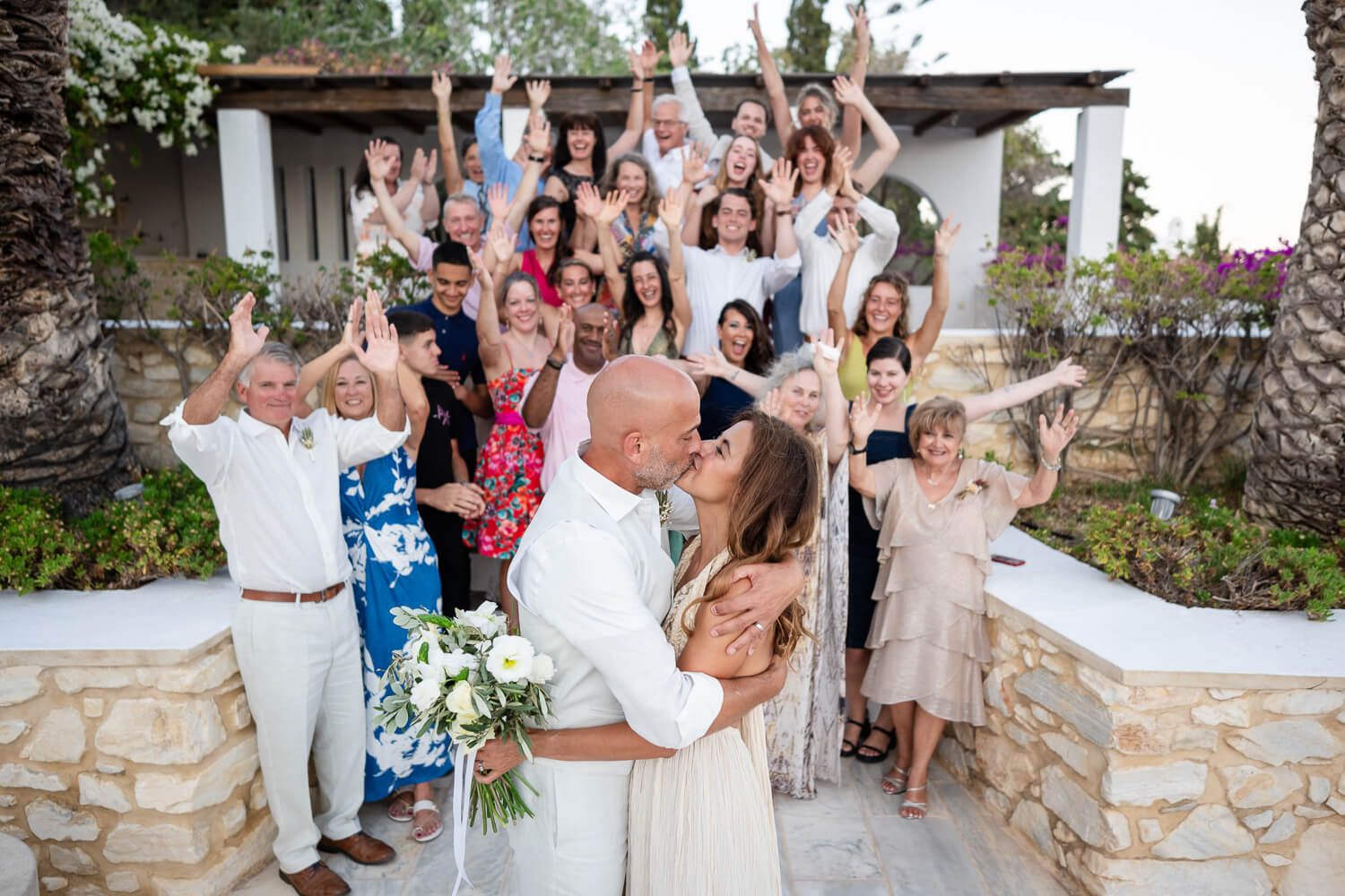 Wedding guests gather outdoors for group photos at a rustic stone venue during a summer celebration.