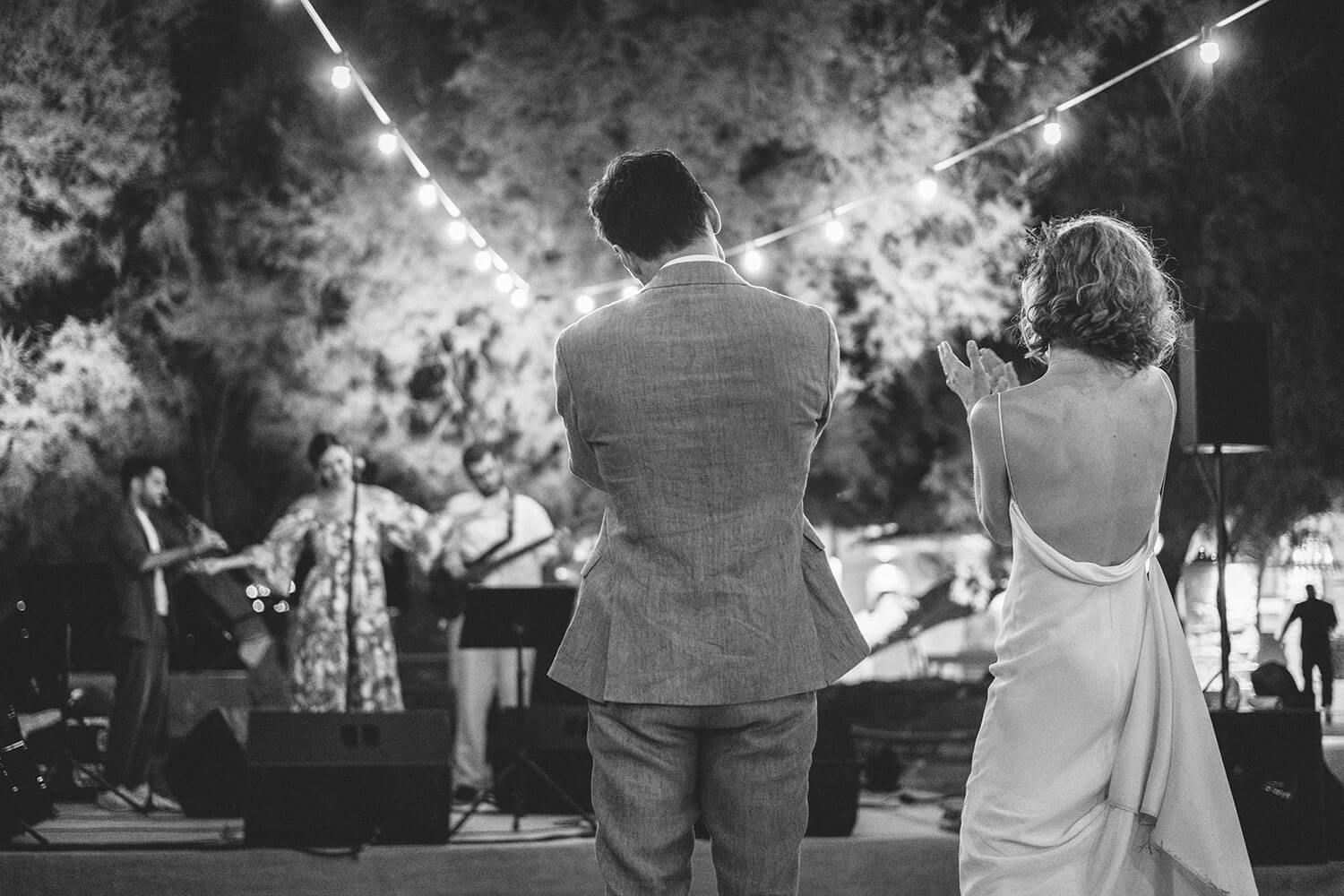 A black and white photo series showing a couple sitting together at an outdoor evening event with string lights overhead.