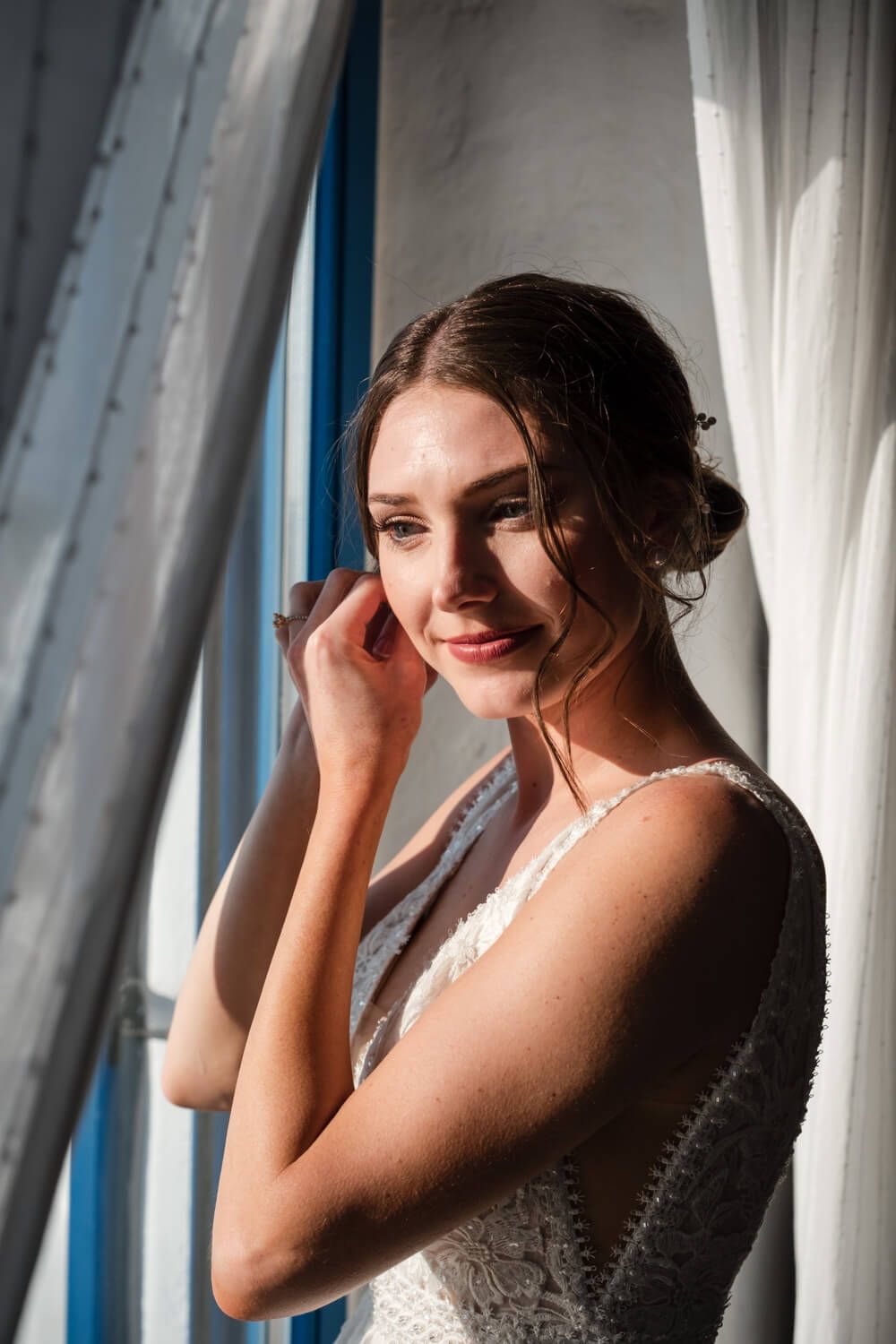 Bride in a white lace wedding dress poses near window light in a sequence of candid expressions.