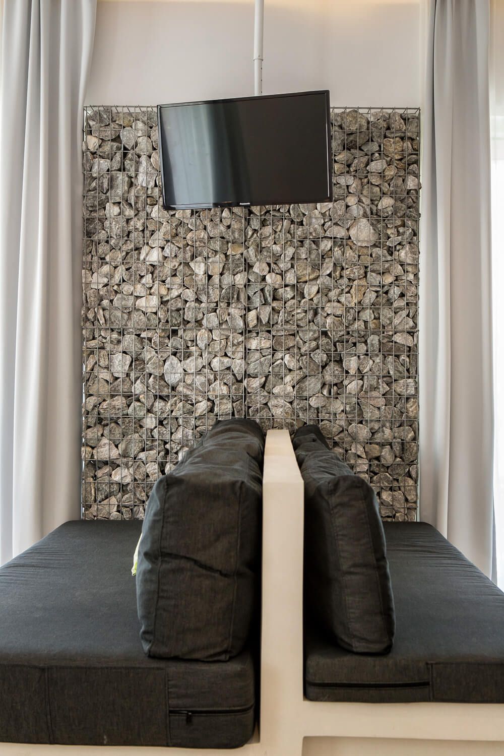 Modern seating area with black cushions against a stone wall backdrop and mounted TV screen.