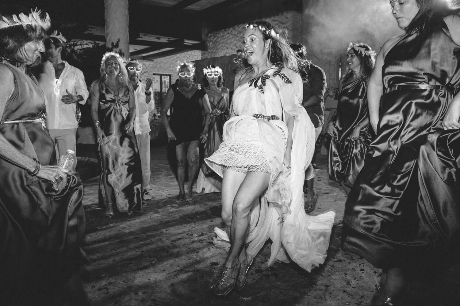 Bride dancing energetically with guests in black and white wedding party photo.
