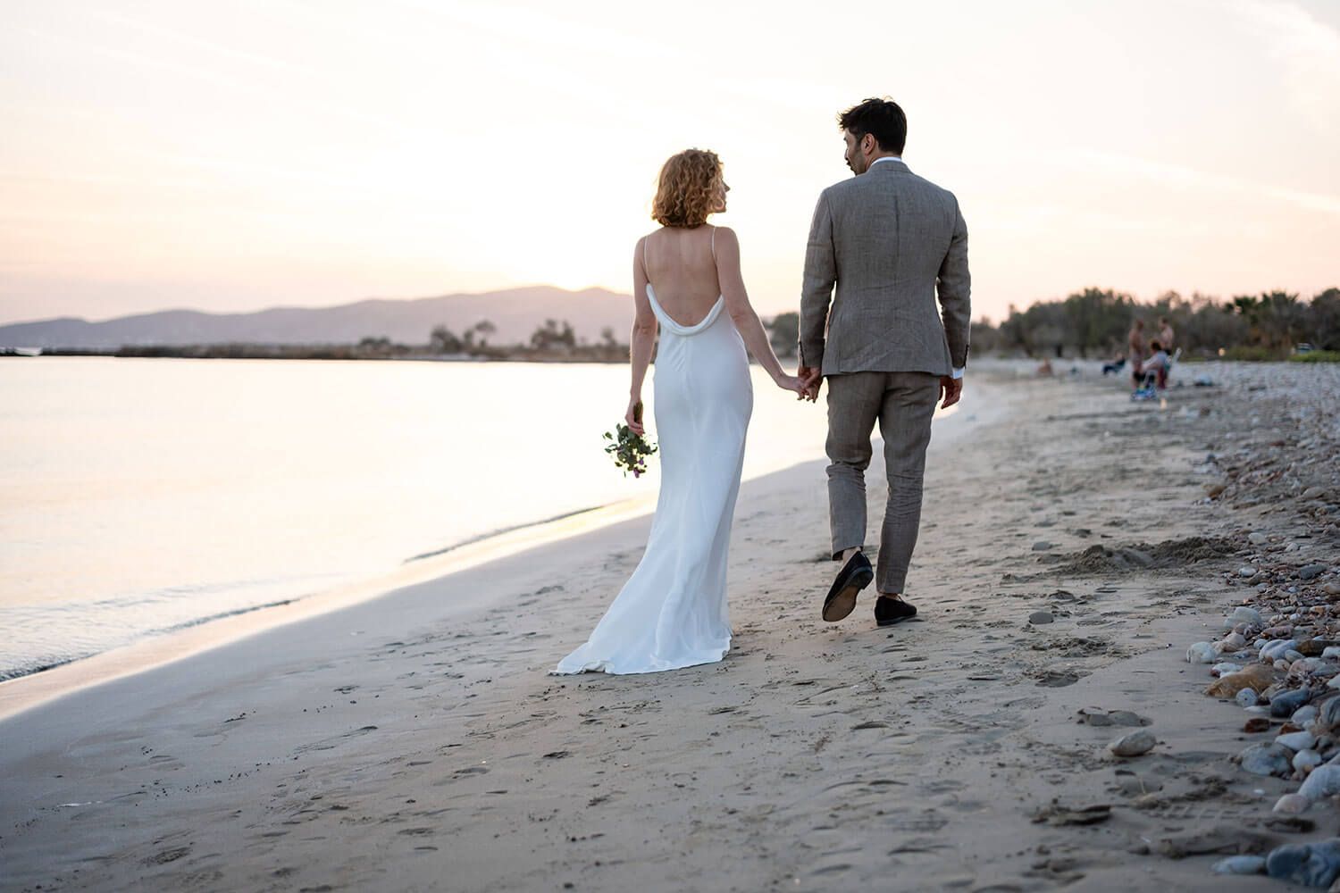 Newlyweds walking hand in hand along the scenic Paros coastline