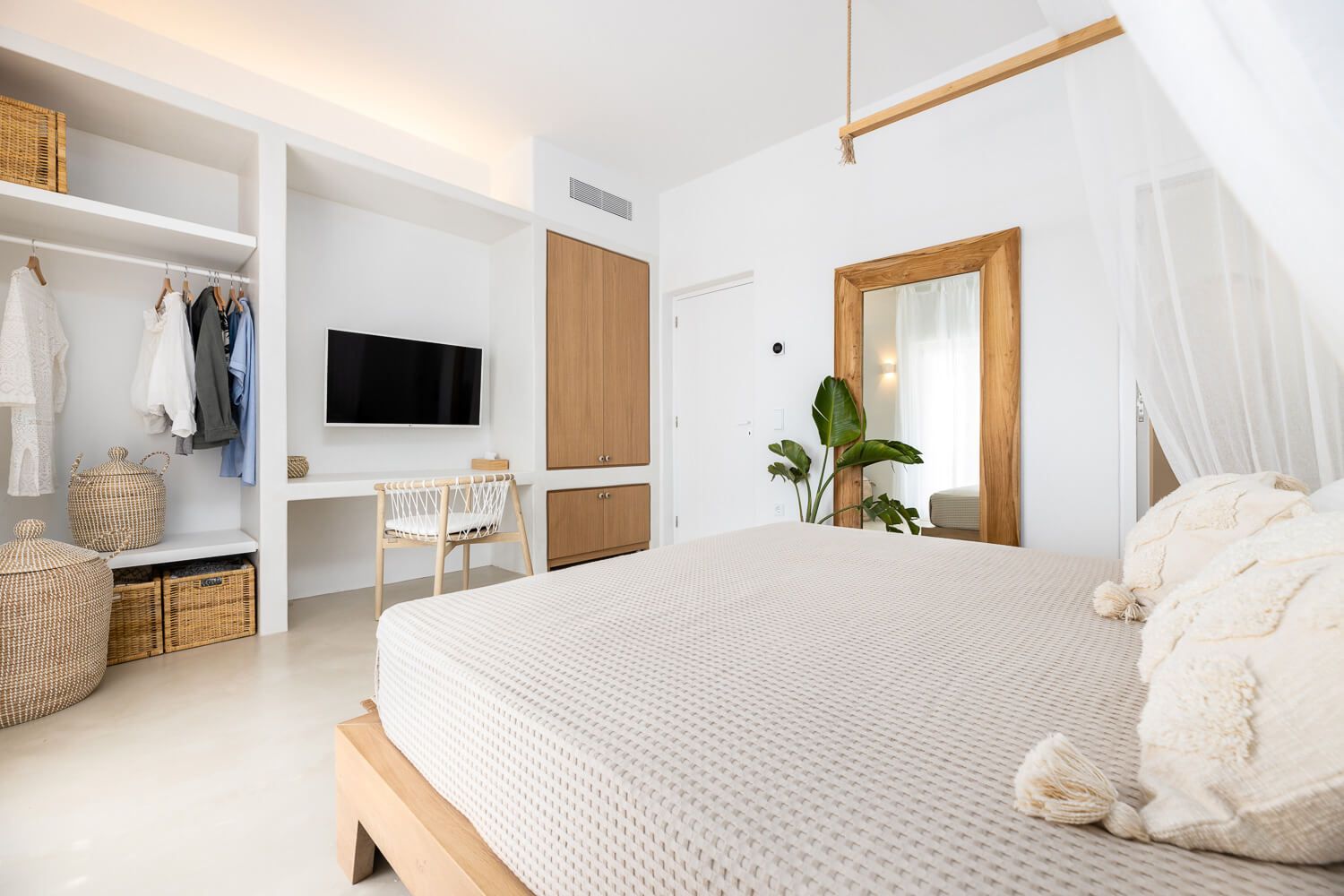 Bright Cycladic-style bedroom with white decor, wooden accents, TV, and open wardrobe storage.