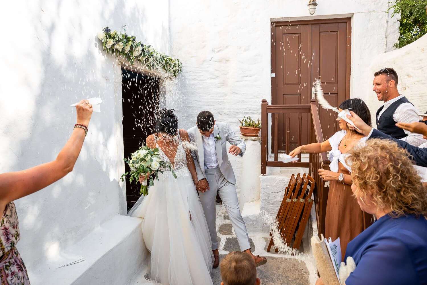 Happy Erika and Marco walking out of the church as guests throw rice and petals