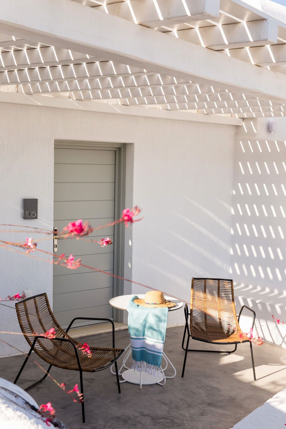 Modern patio with wooden rocking chairs, white fire pit, and pink floral garland creating a cozy outdoor seating area.