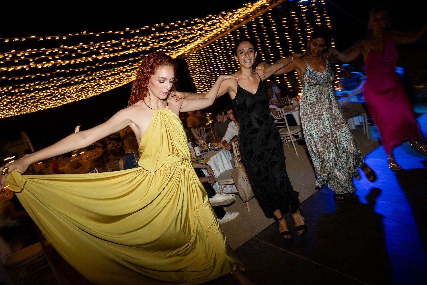 Party guests dance under twinkling string lights at a wedding reception in Syros.