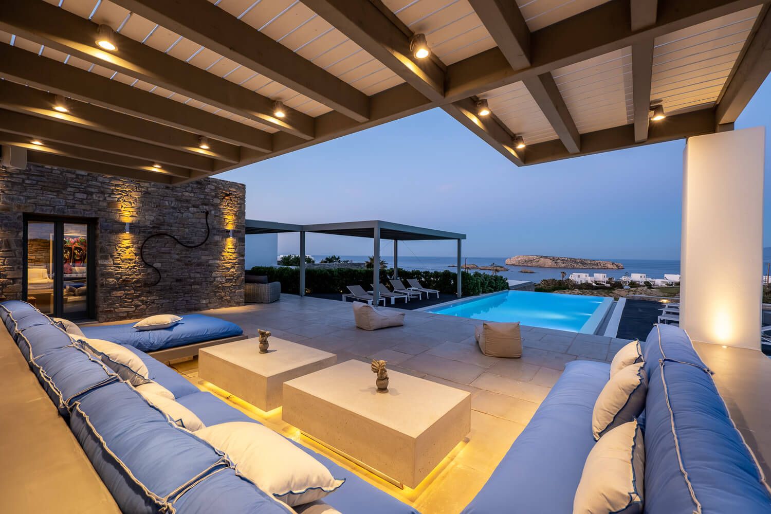 Modern luxury villa exterior with exposed wooden beams and panoramic ocean views at dusk.