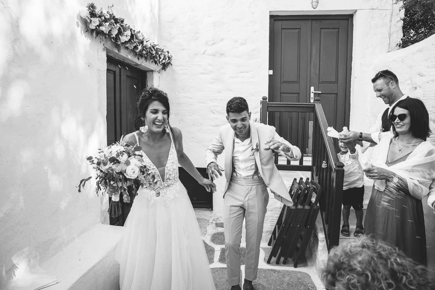 Happy Erika and Marco walking out of the church as guests throw rice and petals