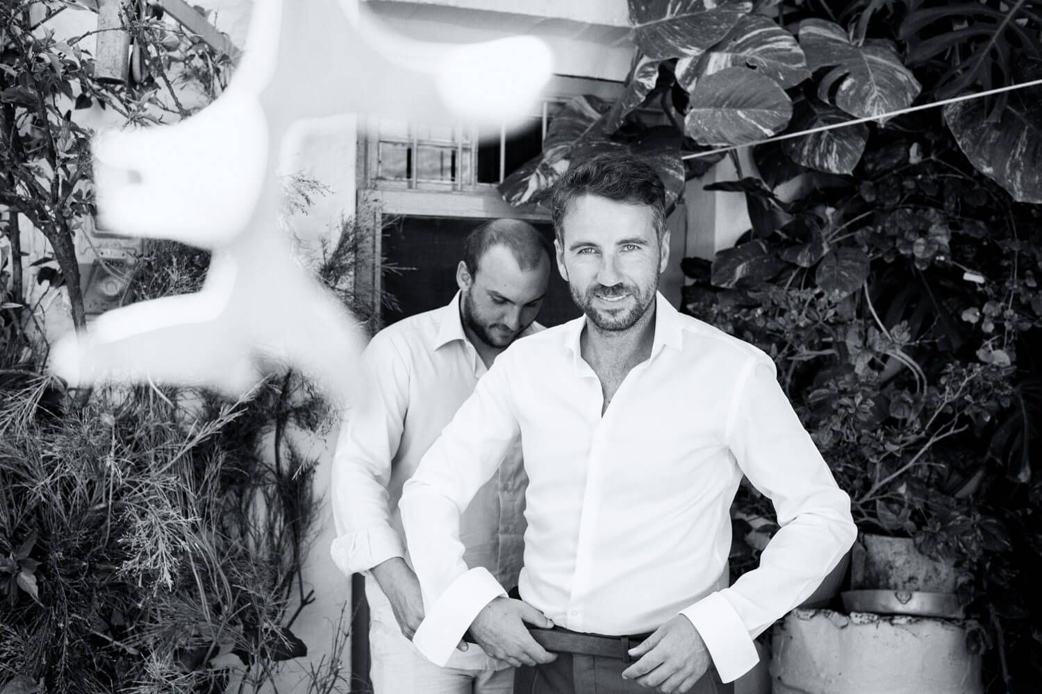 Black and white photo of groom putting on his jacket - Milos wedding