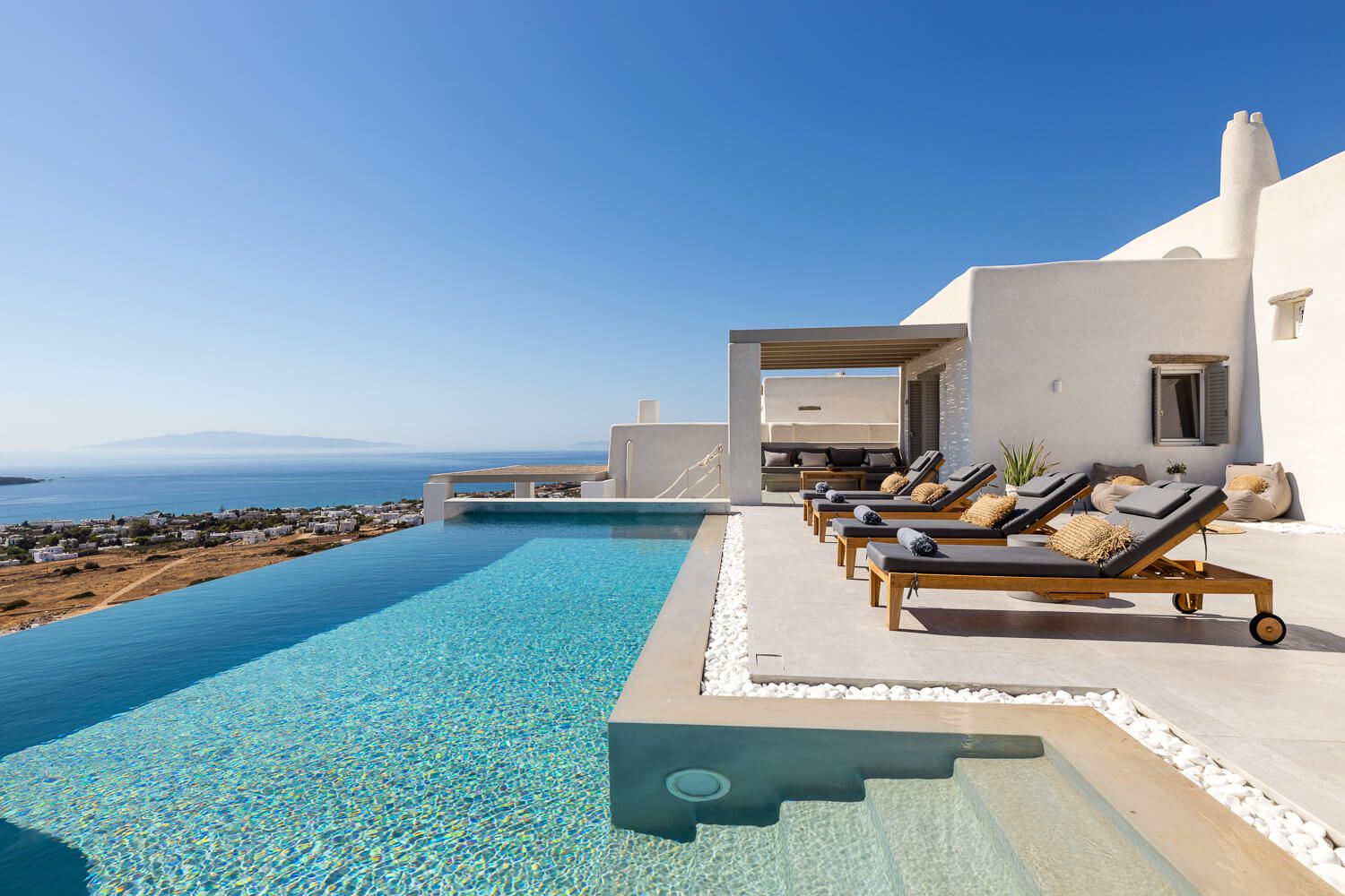 Luxury infinity pool with sun loungers overlooking the Aegean Sea at a stunning Greek island villa.