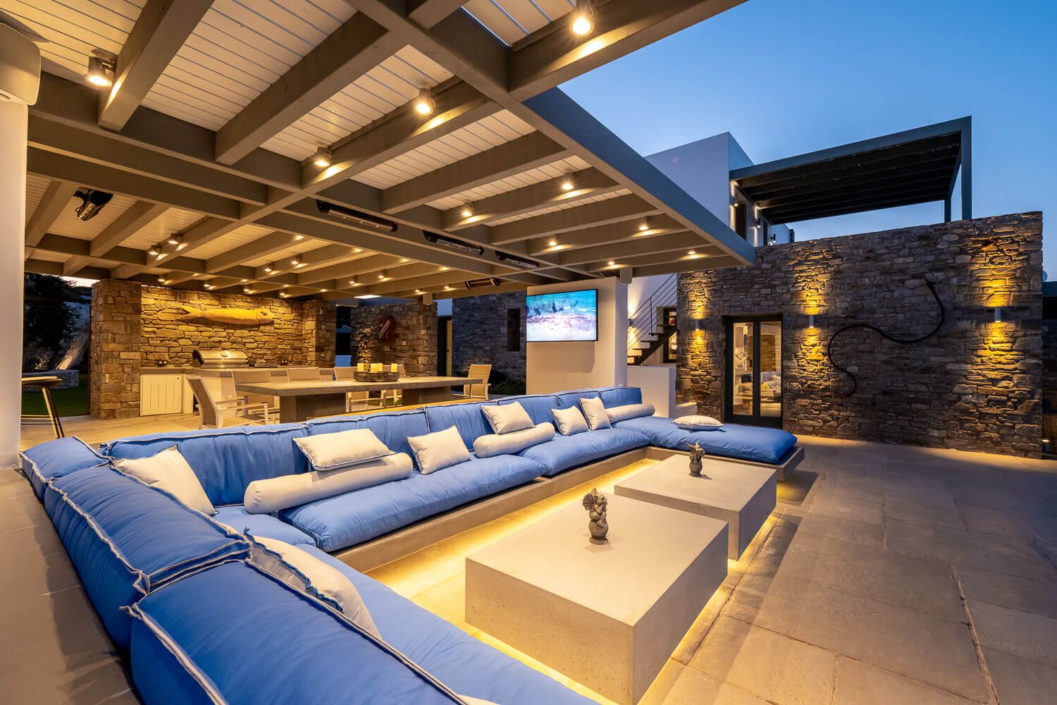 Luxurious outdoor patio with blue sectional sofa and stone walls illuminated by warm lighting at dusk.