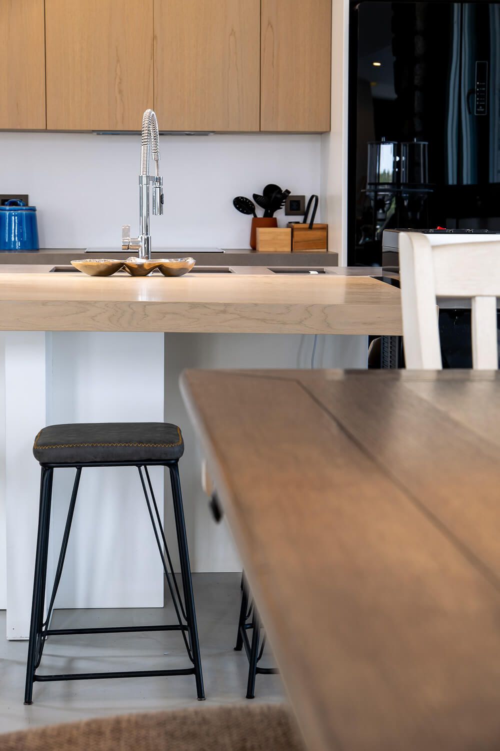 Modern kitchen interior with wooden cabinets, black bar stools, and a sleek countertop in a minimalist design.