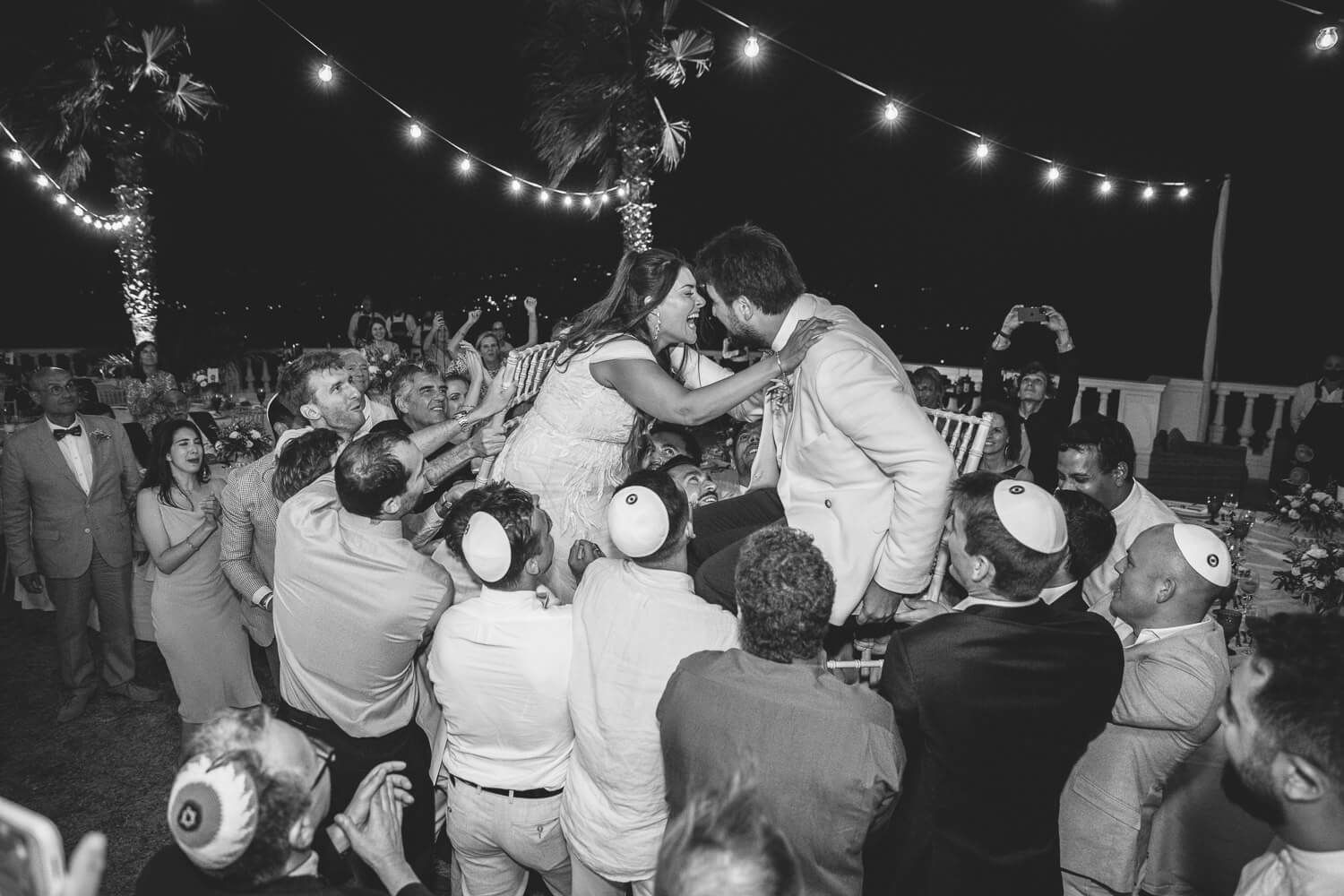 Groom and bride lifted on chairs during Hora dance at Villa Aethra