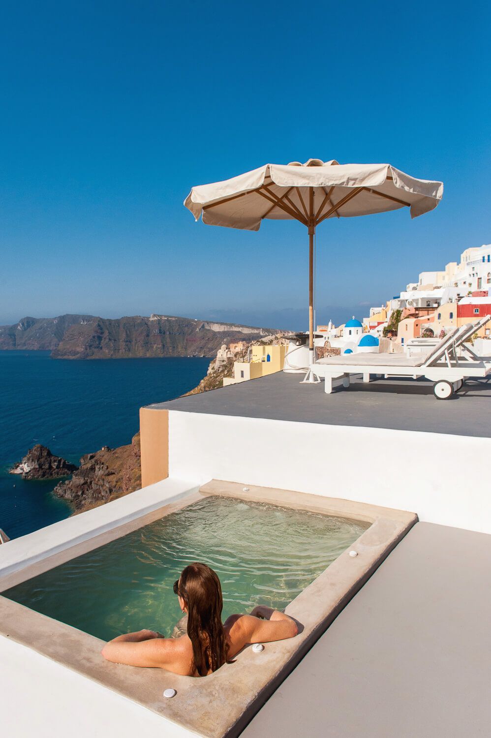 Woman relaxing in a private plunge pool with stunning Santorini caldera and Oia village views.