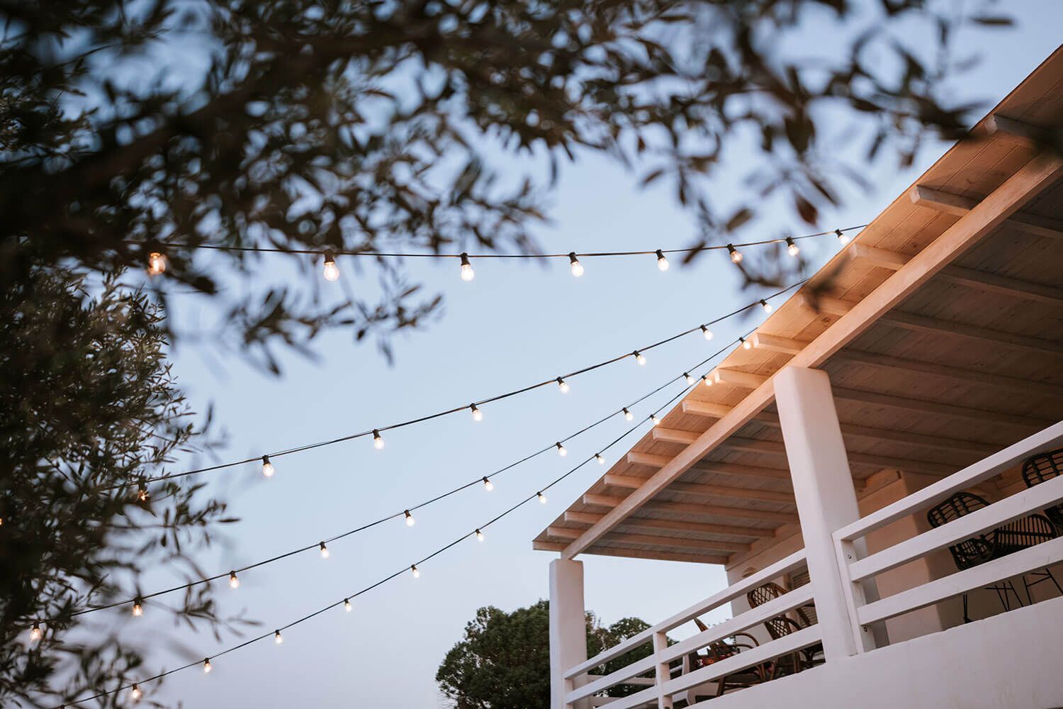 String lights hang between white posts on a wooden deck creating a cozy outdoor ambiance at dusk.