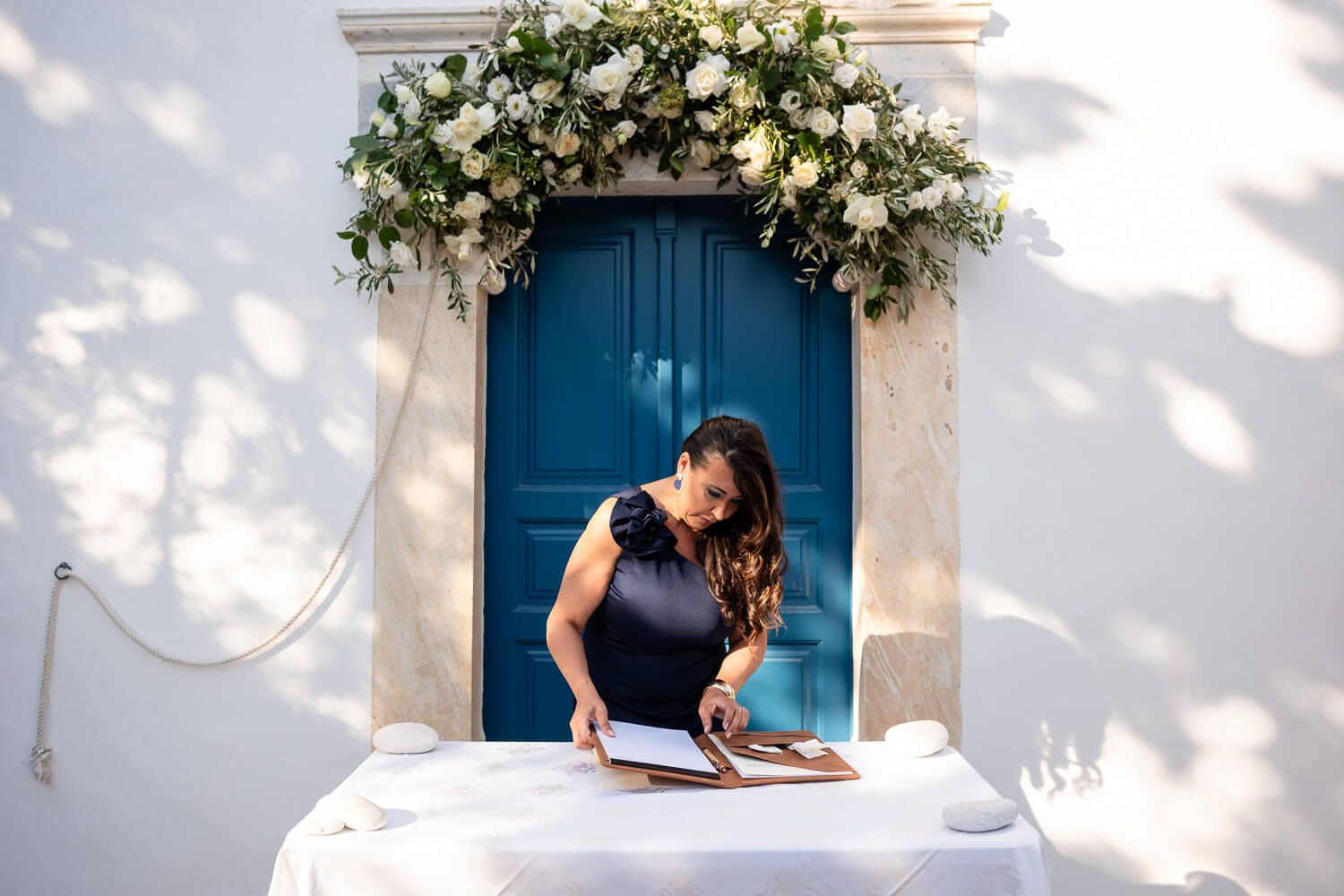 White floral arrangements adorn a Mediterranean-style building with bright blue shutters and doors.