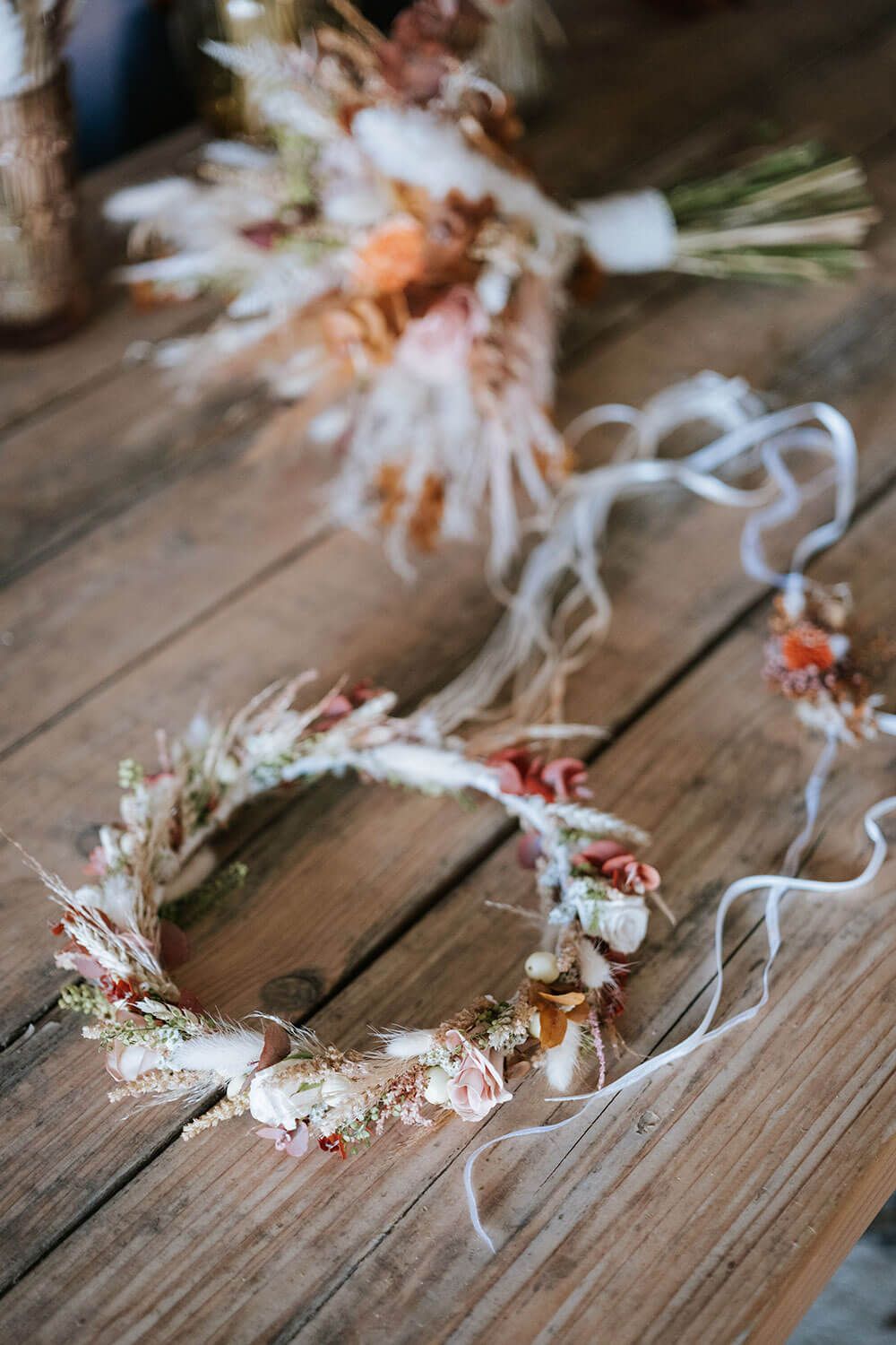 A delicate floral crown with white and peach dried flowers lies on a rustic wooden surface.