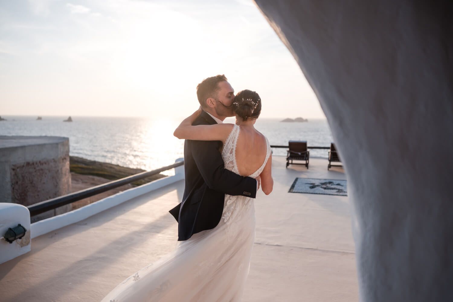 Groom Cody kissing his bride's forehead under the Cycladic sun