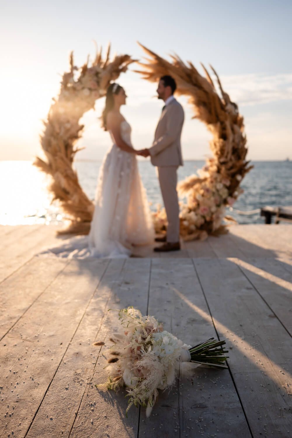 Bride and groom exchange vows at sunset on a pier with bridal bouquet in foreground in Greek island.