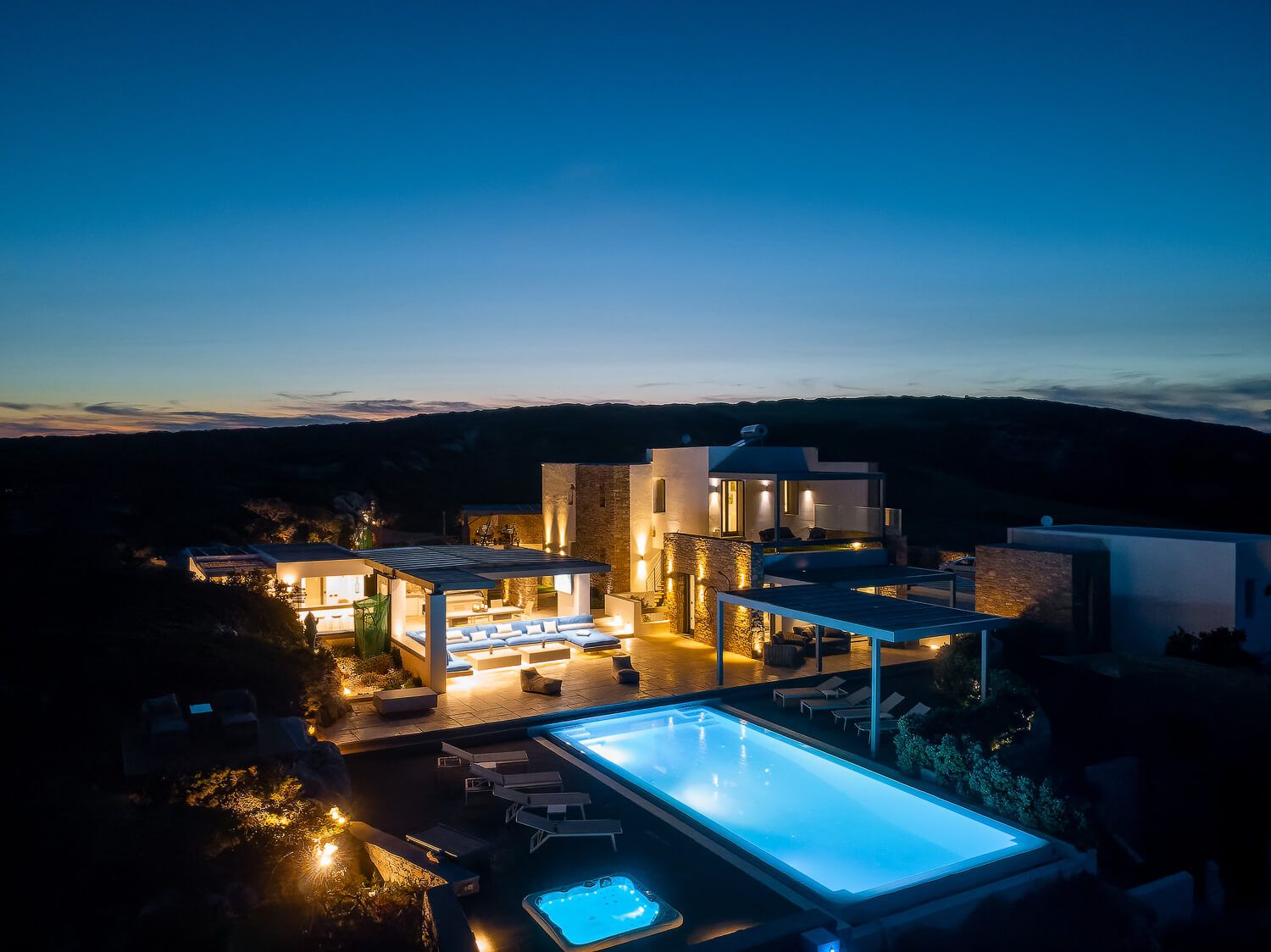 Luxurious villa with illuminated infinity pool overlooking the Aegean coast at twilight.