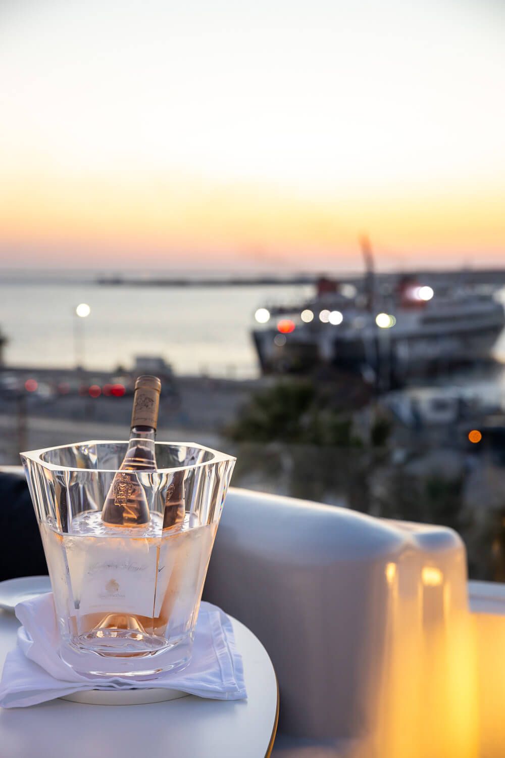 A bottle of rosé wine chills in an ice bucket at sunset overlooking Parikia Port