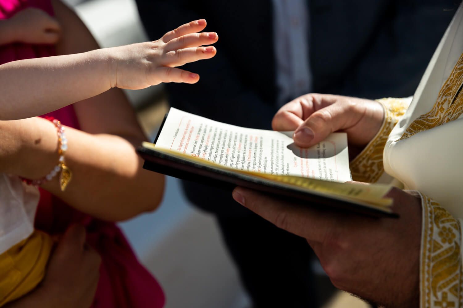 Priest blessing a baby during a religious baptism ceremony outdoors.
