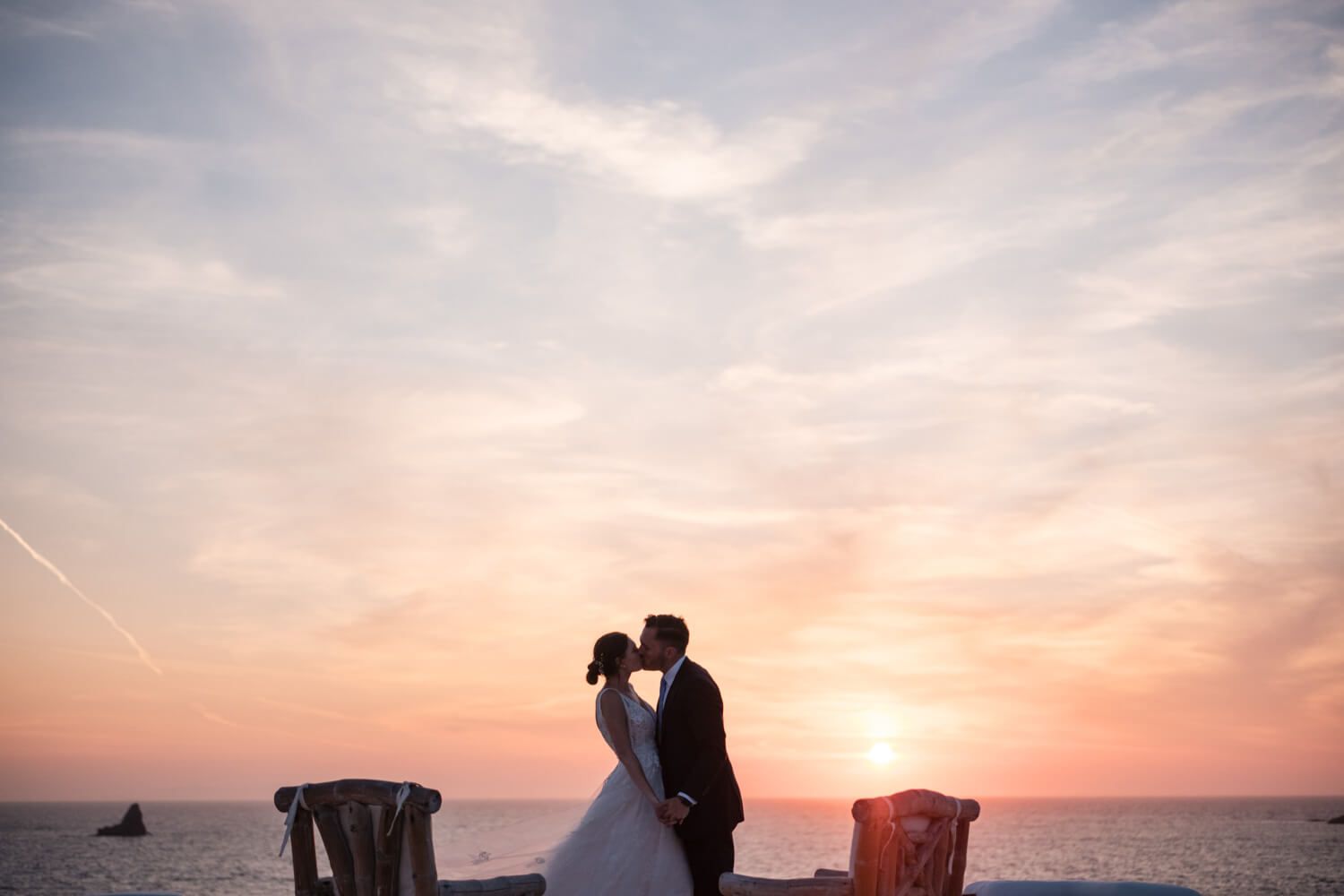 Bride and groom share sunset kiss with vibrant pink and orange sky backdrop at Villa Lady of Paros.