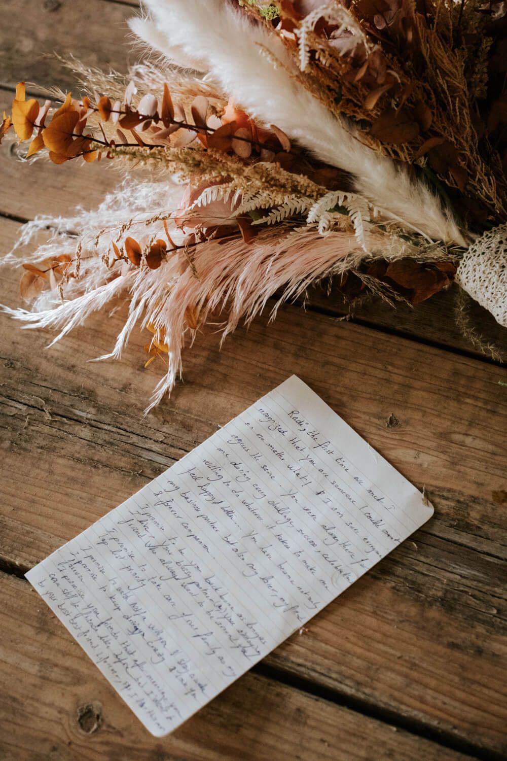 Handwritten wedding vows on rustic wooden table with dried floral arrangement.