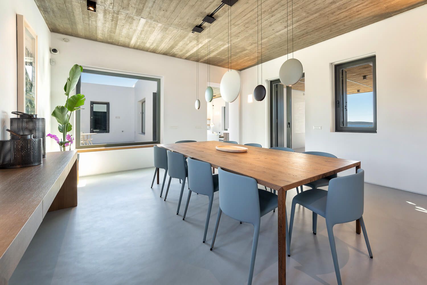 Modern dining room with wooden table, concrete ceiling and pendant lights in a Cycladic Villa.