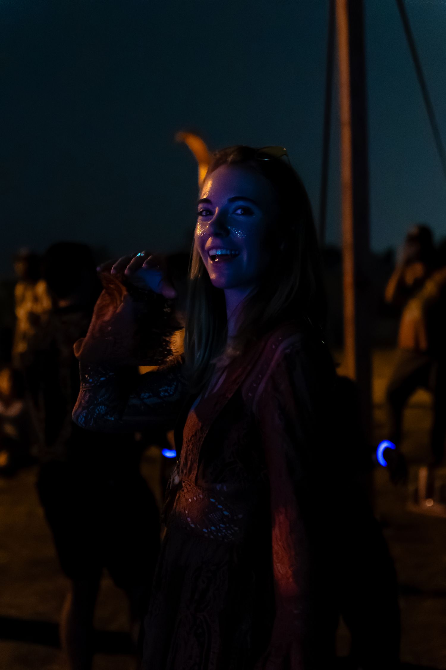 Femme souriante avec des paillettes sur le visage danse dans la foule sombre à l’Anatha Fest à Montréal, regardant la caméra.