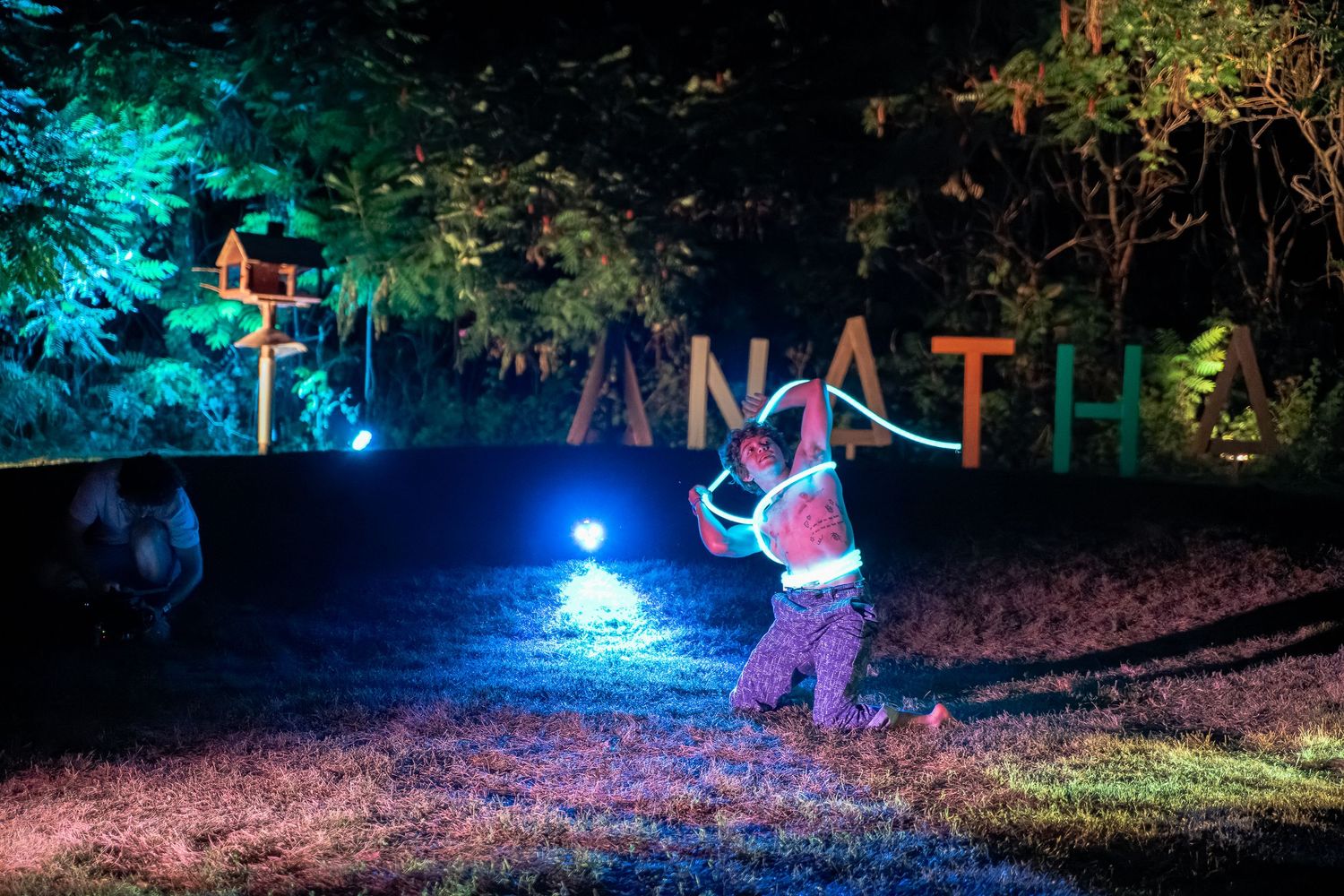 Le soir à l’Anatha Fest à Montréal, un homme danse avec une corde lumineuse devant l’enseigne illuminée du festival.