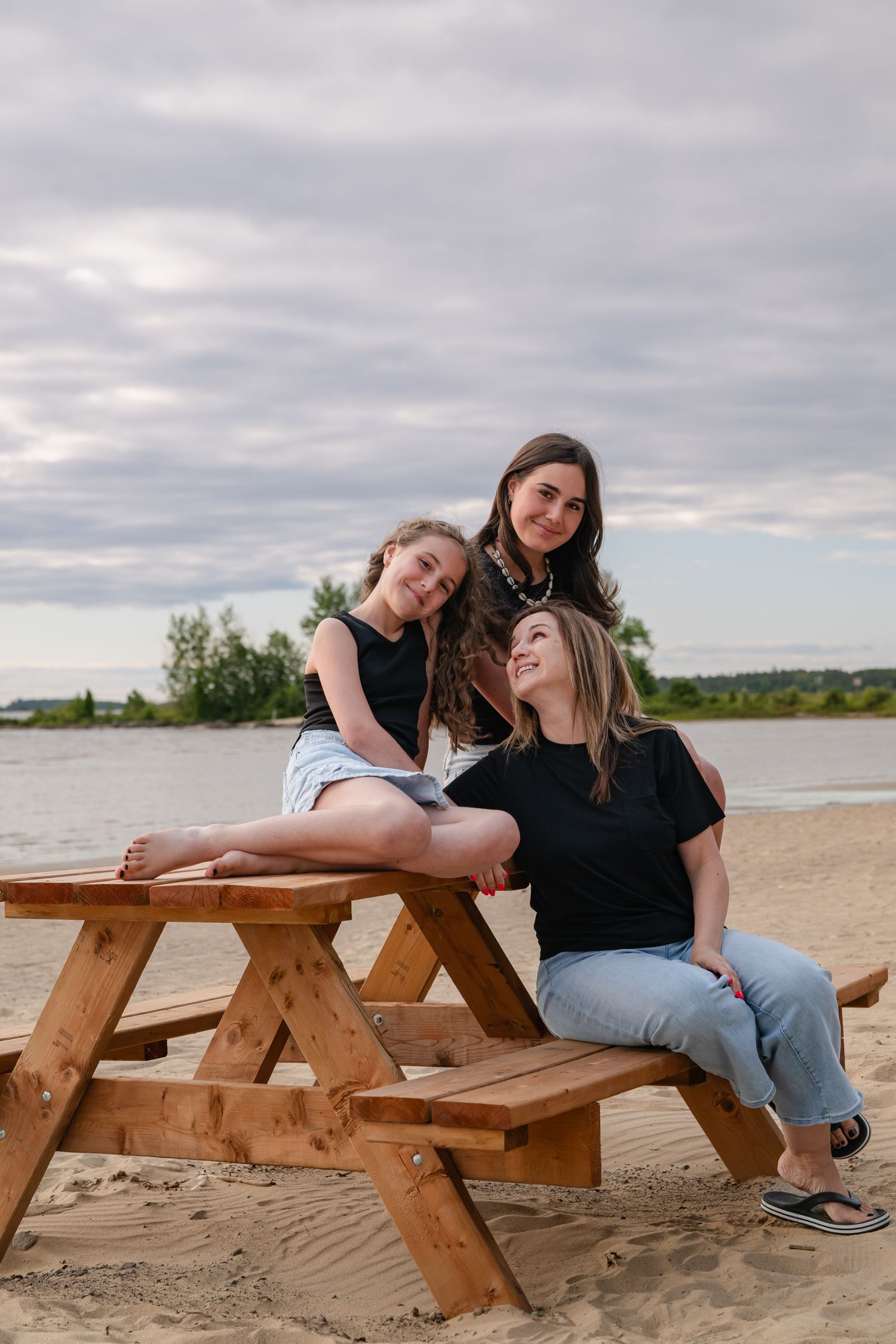 Maman avec ses deux filles adolescentes assises à une table de pique-nique à la plage de Saint-Gédéon, moment complice et souriant