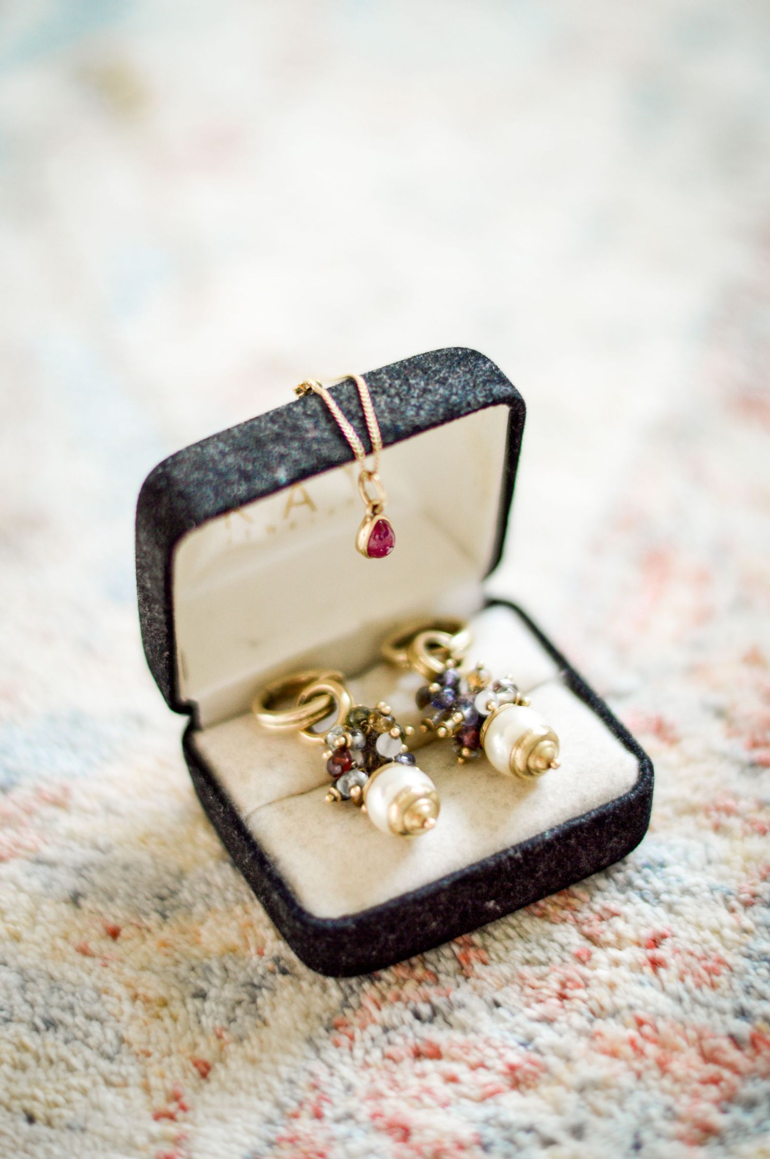 Zarte Ohrringe aus Perlen und Diamanten in einer Schmuckschatulle aus schwarzem Samt mit einem Rubinanhänger als Detail.