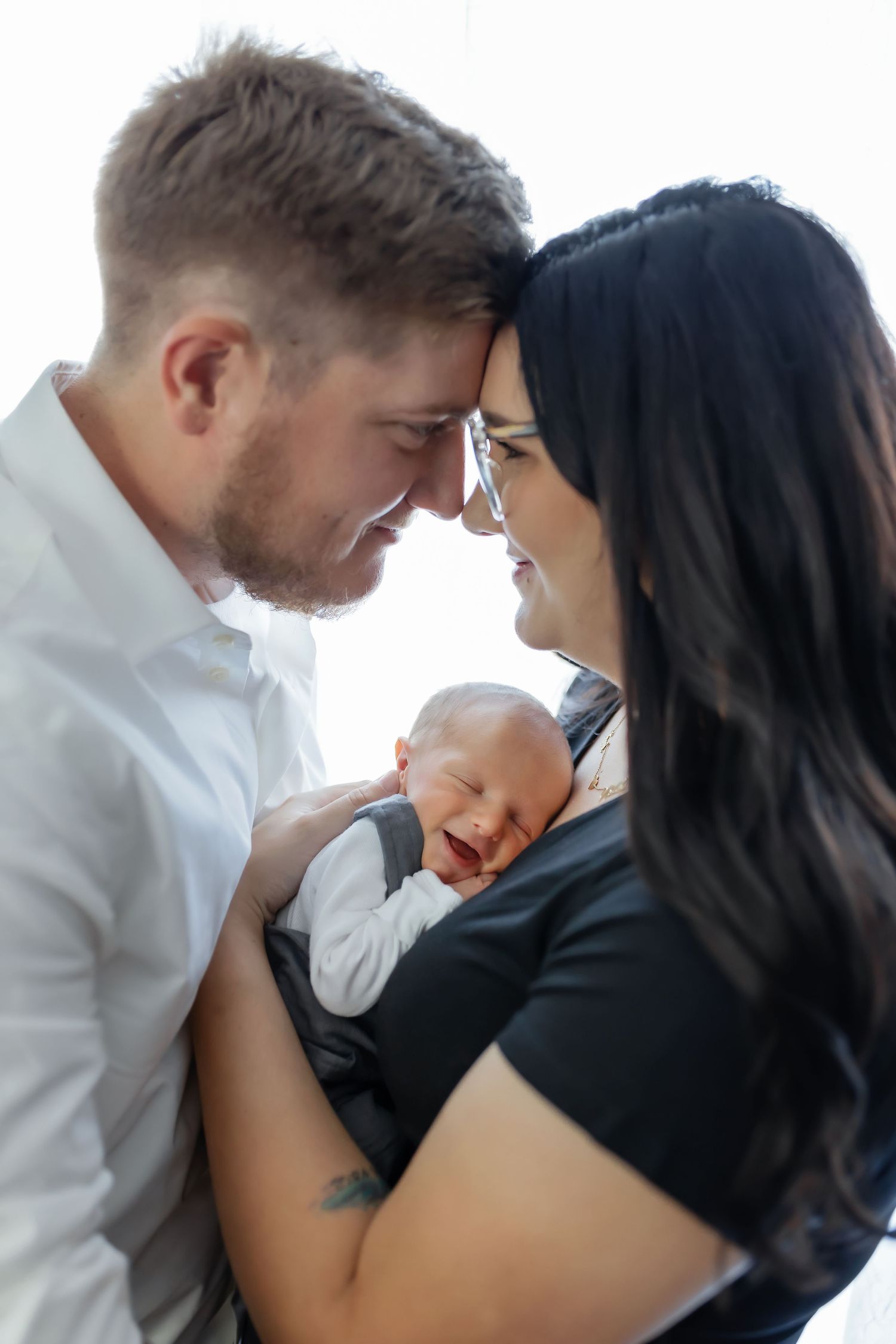 Intimate family portrait with newborn baby between parents touching foreheads.