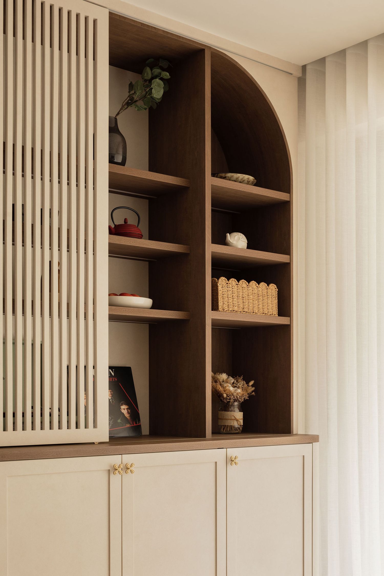 Elegant built-in wooden bookcase with arched shelving, decorative items, and cream cabinet doors with brass hardware.