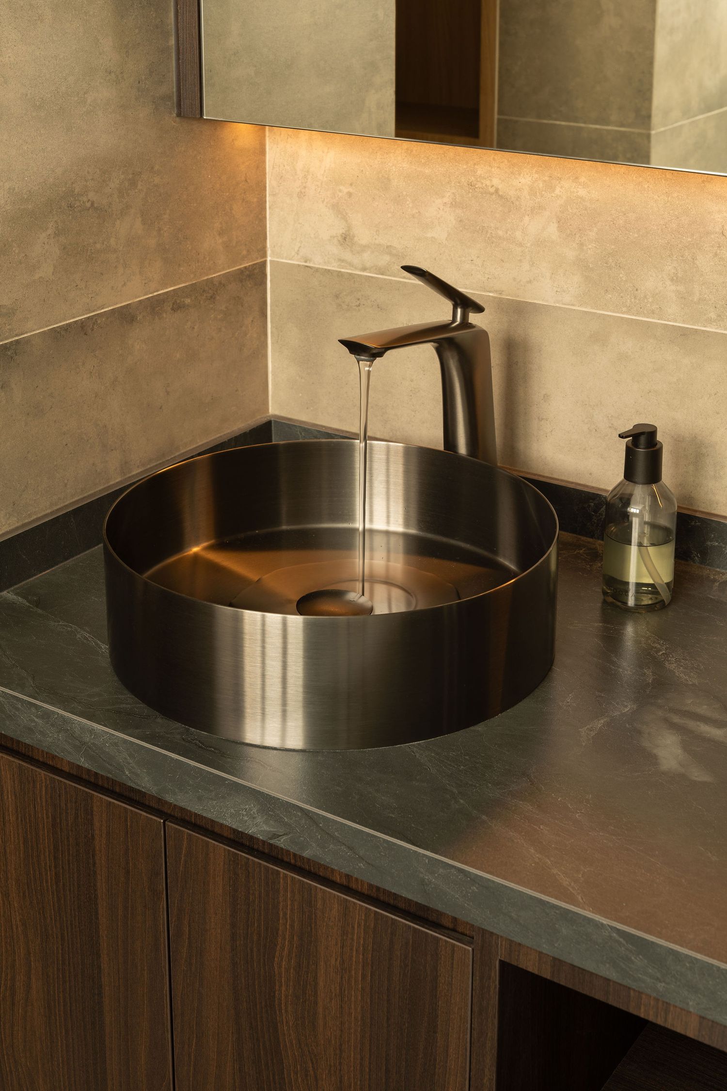 Modern bathroom featuring a round brushed bronze vessel sink with matte black faucet on a dark stone countertop.
