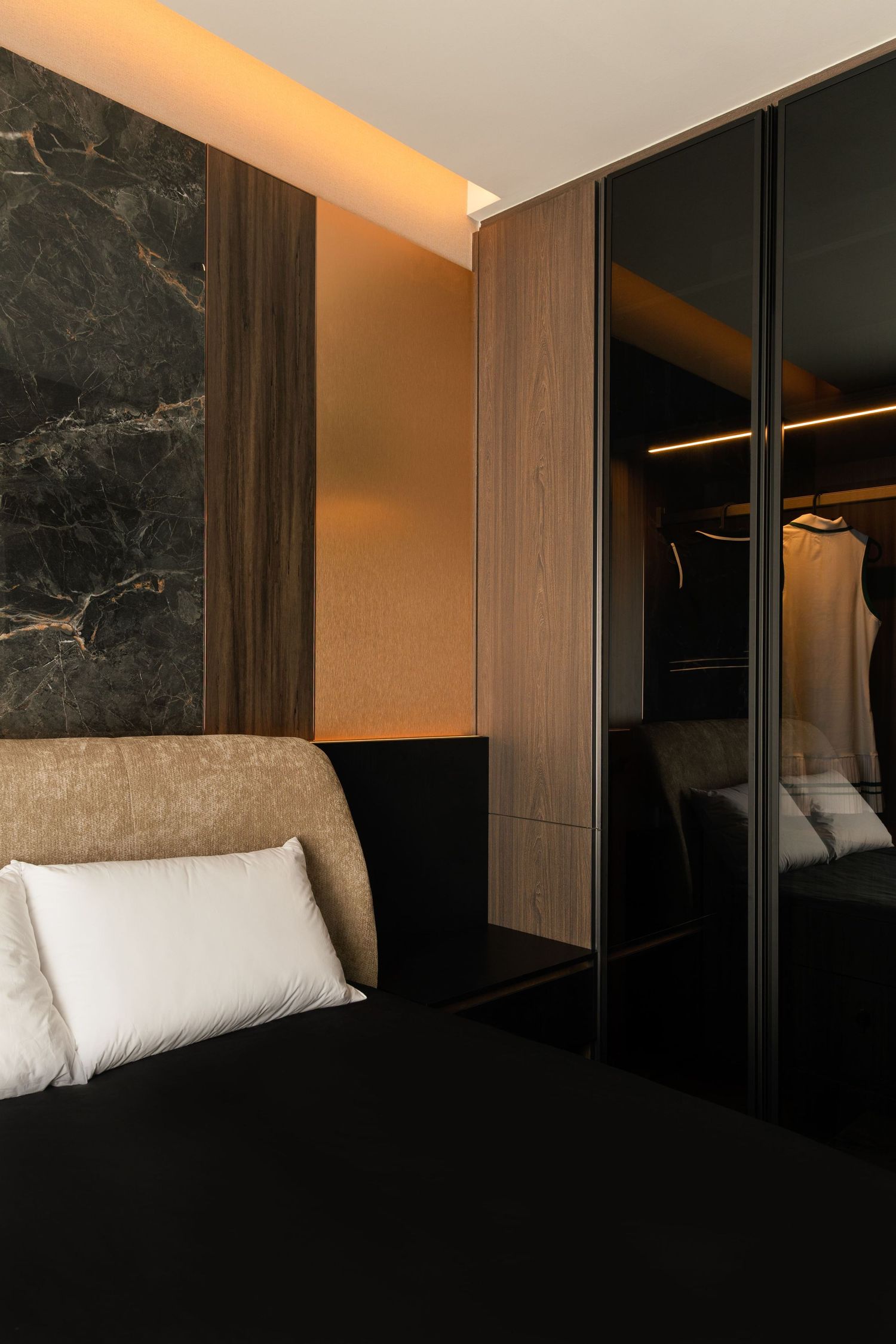 Luxury bedroom with black marble wall, warm LED lighting, mirrored wardrobe, and elegant dark bedding with white pillows.