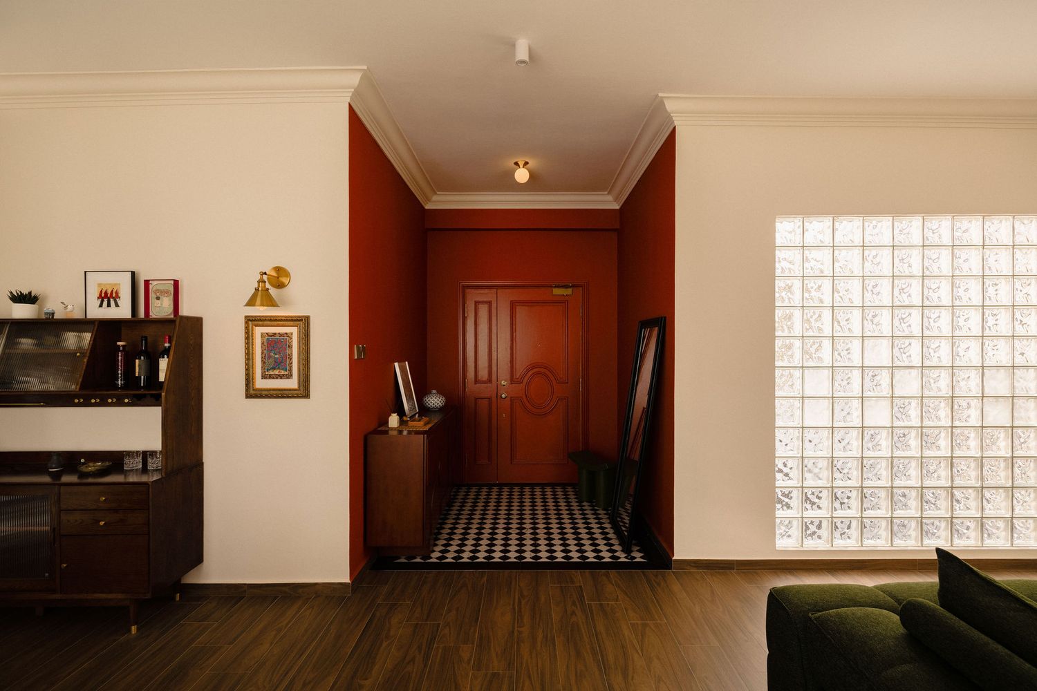 Warm retro entryway with terracotta red walls, a checkered tile floor, a wooden door, a glass block window and a vintage wooden cabinet.