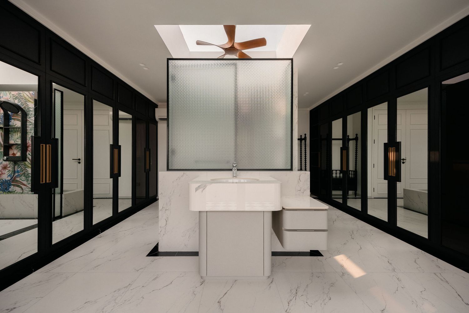 Luxury marble bathroom with black-framed glass cabinetry, a freestanding vanity, frosted glass partition, skylight and wooden ceiling fan.