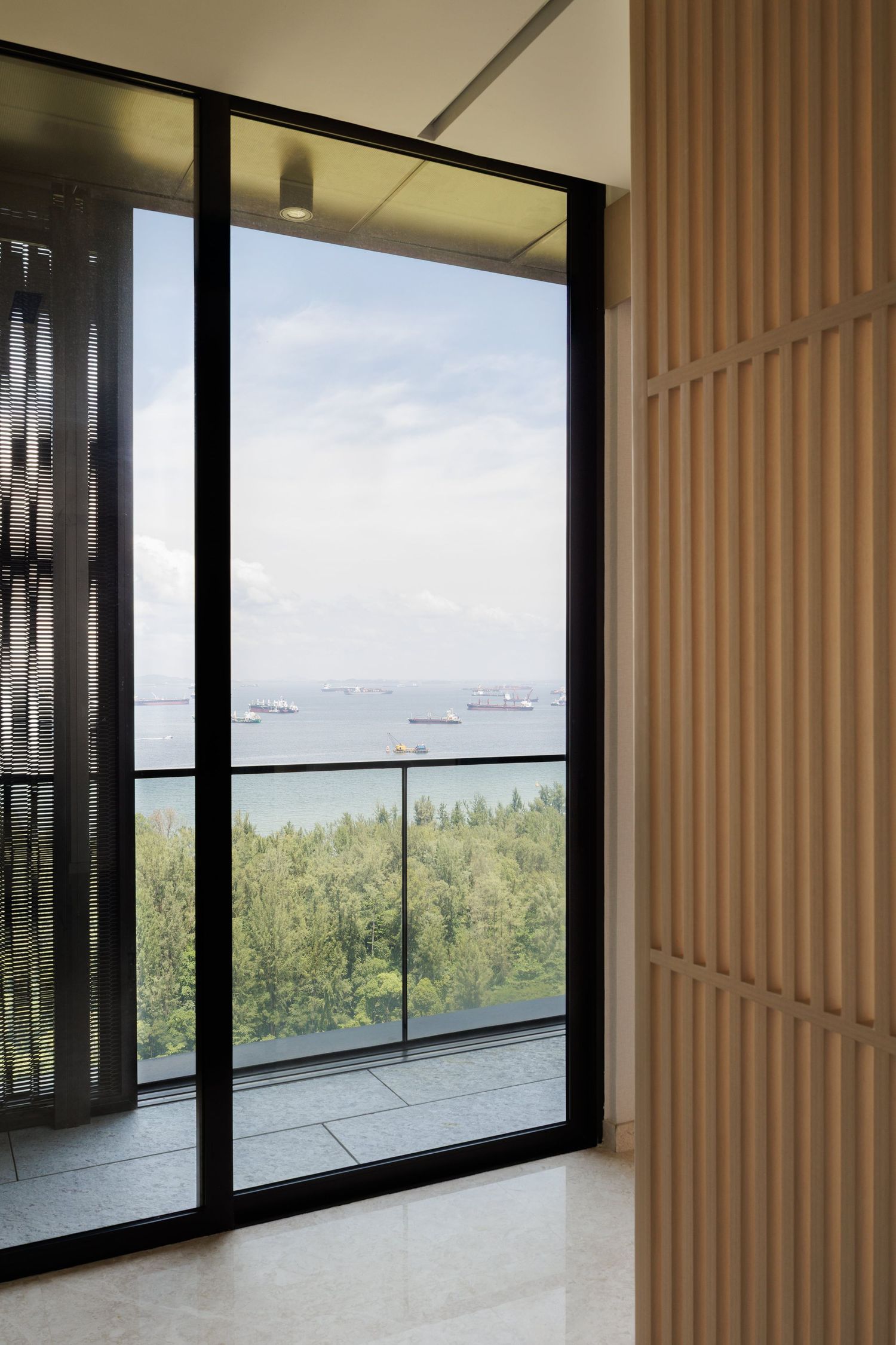 Modern apartment interior with floor-to-ceiling windows offering panoramic views of a green landscape and distant harbor.