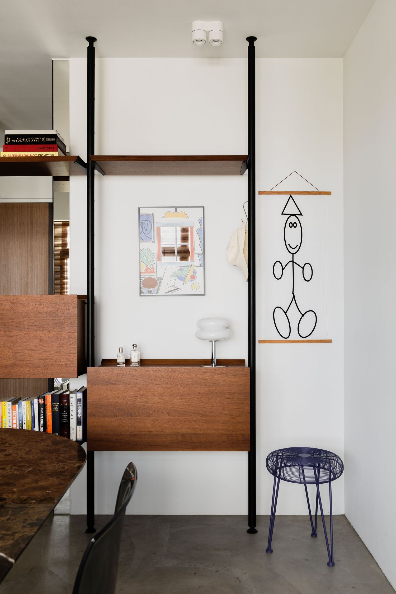 Modern interior design featuring wall-mounted shelving unit with wood panels, abstract art, and a blue metal stool.