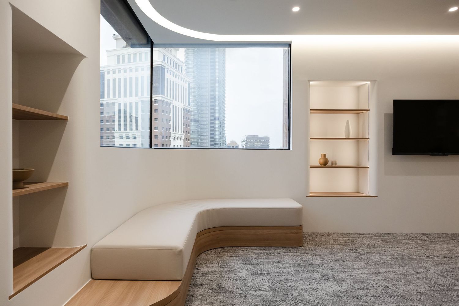 Modern office interior with minimalist white walls, built-in shelving, and gray carpeting in an open floor plan space.