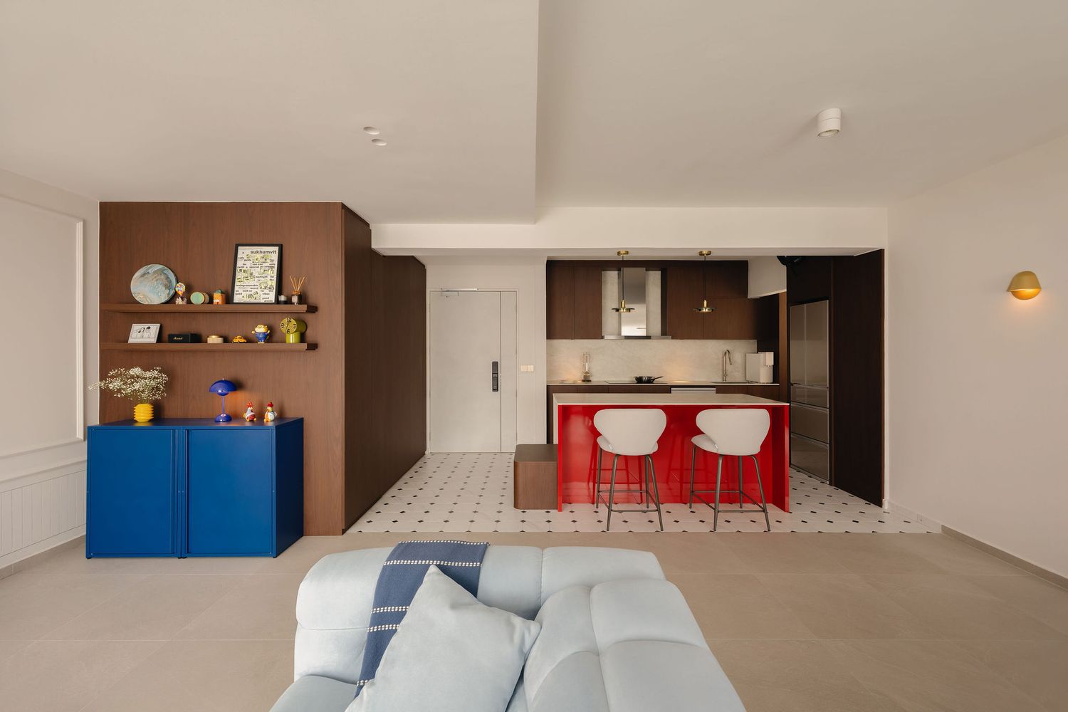 Modern open-plan living room with blue cabinet, red kitchen island, bar stools, and patterned tile flooring.