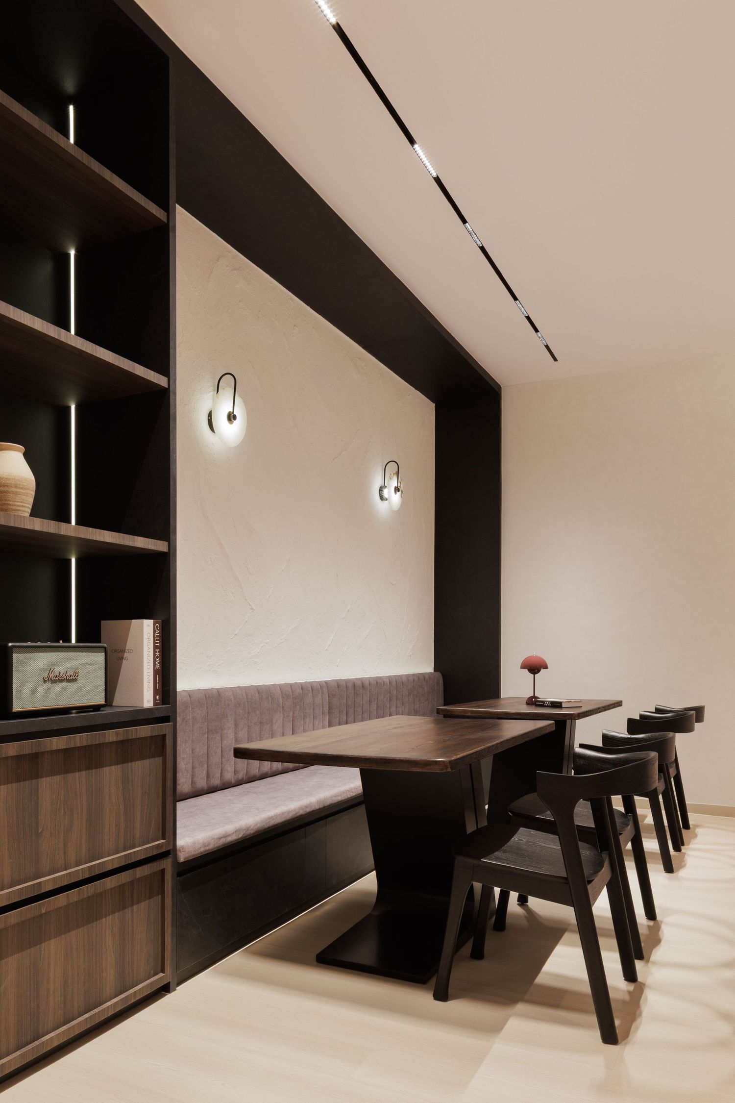 Modern minimalist dining space with built-in wooden bench seating and black chairs along a neutral-toned wall.