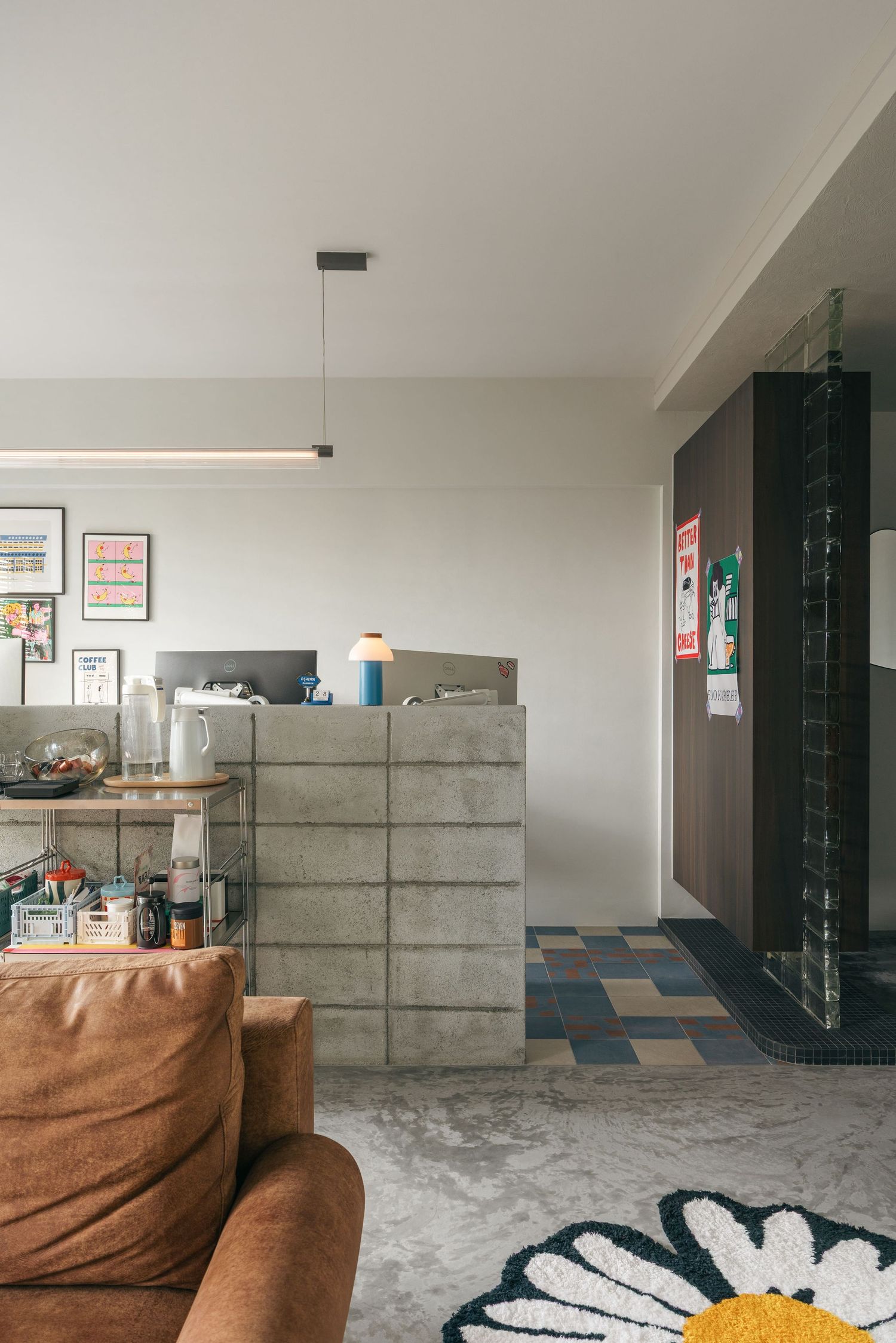 Modern living room with concrete block divider, brown leather sofa, floral rug, and colorful tile flooring.